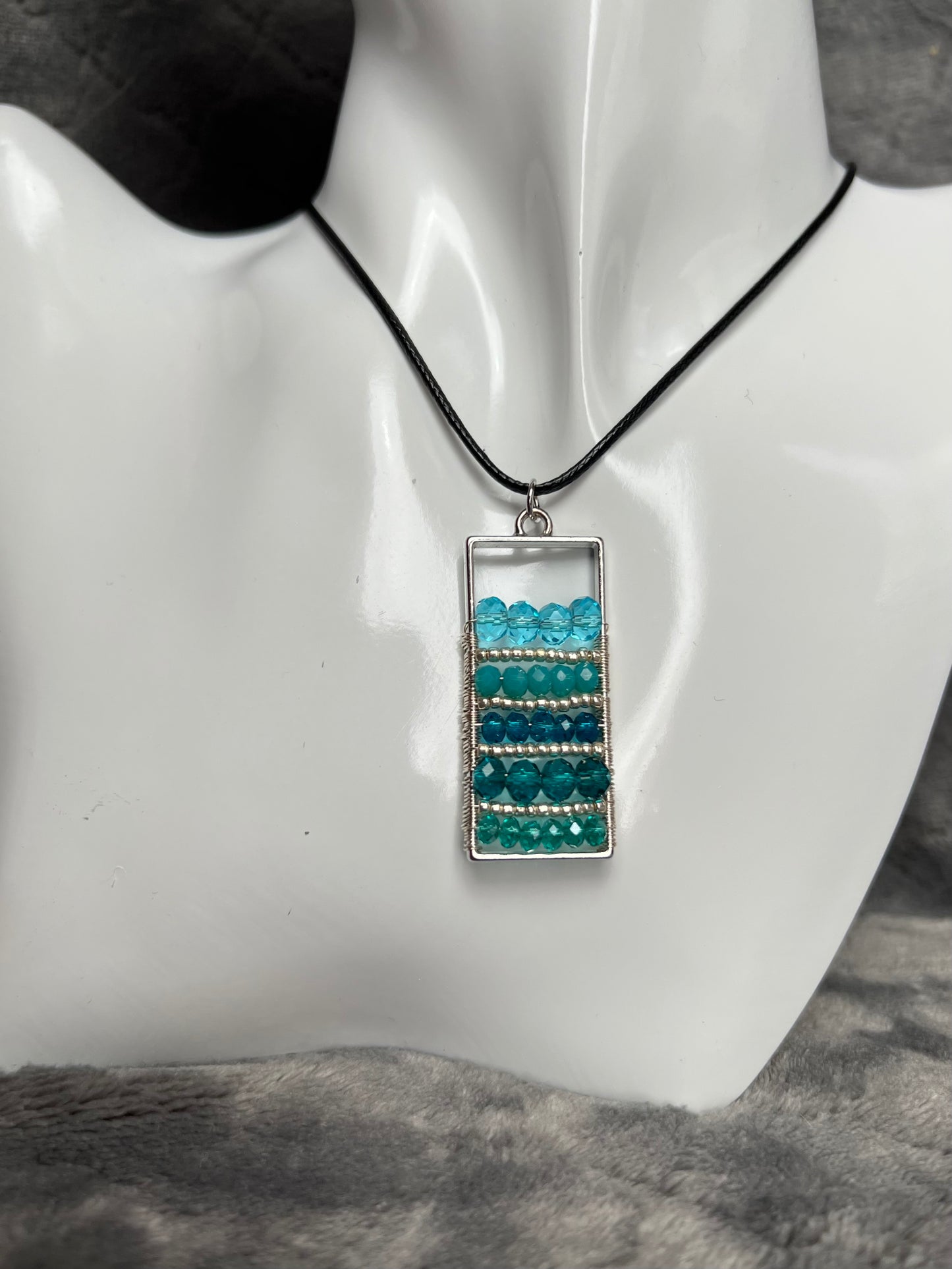 Necklace- Waxed cotton cord with silver plated metal and clasp with various shades of turquoise colored crystals.