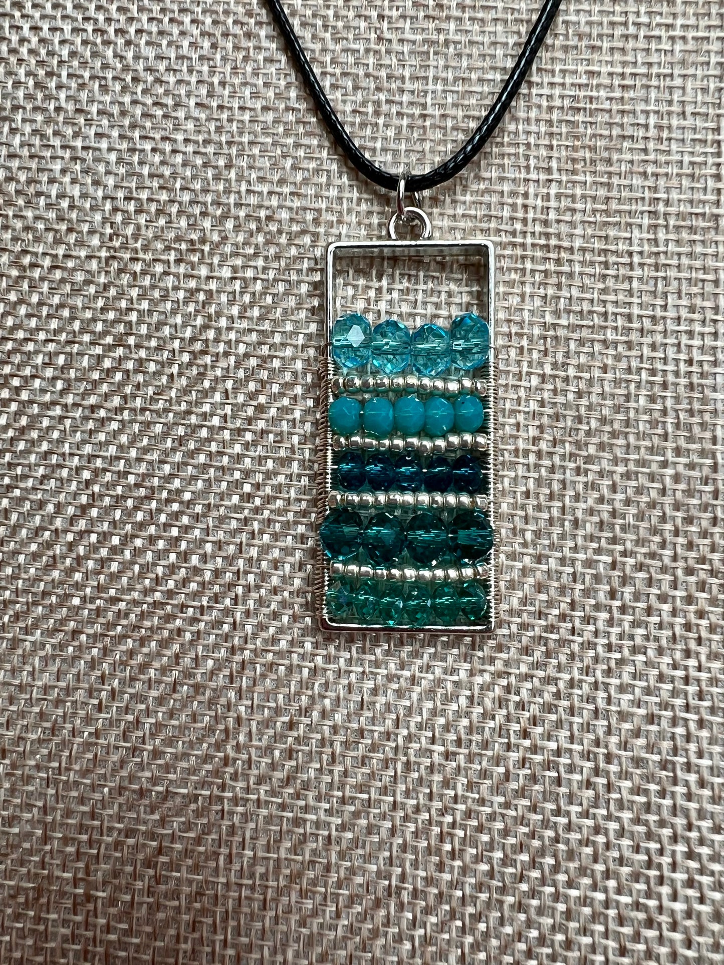 Necklace- Waxed cotton cord with silver plated metal and clasp with various shades of turquoise colored crystals.